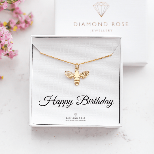 Gold bee necklace in a 'Happy Birthday' card with Diamond Rose Jewellery branding, surrounded by pink flowers.