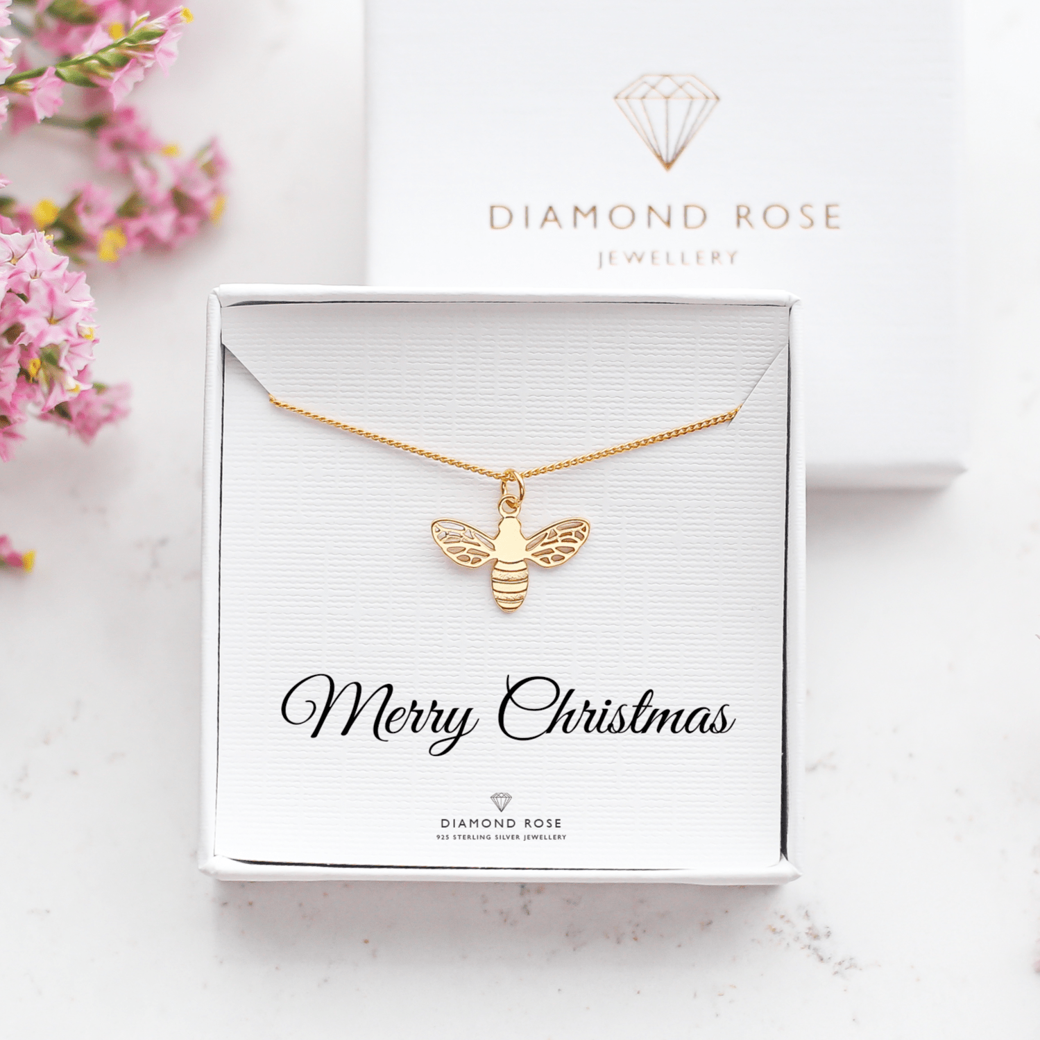 Gold bee necklace in a 'Diamond Rose' box with pink flowers around